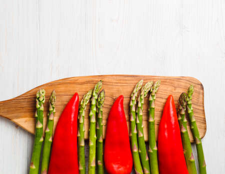 Fresh vegetables - green asparagus and red peppers on a cutting wooden board, top view. Asparagus and peppers alternate. Cooking concept. Copy space.の写真素材