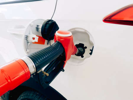 Refueling a car close-up. A red filling nozzle is inserted into the gas tank of a white car.の写真素材