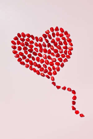 Heart made of red ripe pomegranate seeds on a pink background. heart shaped pomegranate seeds.の写真素材