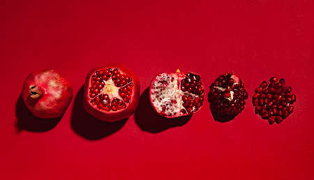 a row of ripe pomegranates on a red background, pomegranates in different stages of cutting, a whole pomegranate, a pomegranate with a cut top, half a pomegranate, a quarter of a pomegranate and seedsの写真素材