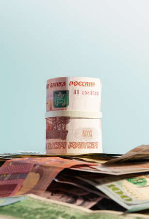 A bundle of Russian paper money in denominations of 1 and 5 thousand rubles, rolled up, lies over USA and European paper money - USD, EUR and GBP.の写真素材