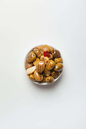 grilled green olives in oil, pitted, with red hot pepper and garlic in a white bowl on a light background, view from aboveの写真素材