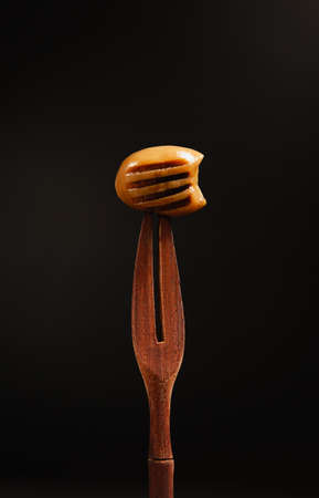a wooden olive skewer for eating olives, on which a green grilled olive is pierced, pitted, on a black background, close-upの写真素材