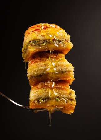 three delicious honey baklavas with pistachios on a fork on a black background, side viewの写真素材