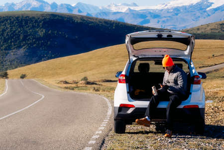 tourist rest - a man sits in the trunk of his car on the side of the road in the mountains, a...