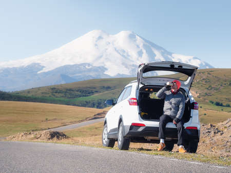 tourist rest - a man sits in the trunk of his car on the side of the road in the mountains, a...