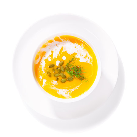 pumpkin soup in a white plate on a white background, top view, orange soup with pumpkin seeds, herbs and cream, isolatedの写真素材
