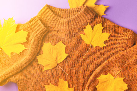 Autumn concept, flat lay - brown knitted sweater and yellow autumn maple leaves on lilac paper,...