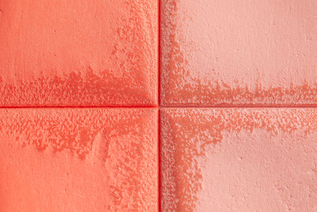 Four red-orange tiles are arranged in a square pattern, each having a slightly different shade and texture. The surface is rough and uneven. Macro shotの写真素材