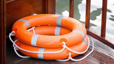 Two wet orange life preservers with white rope sit on a weathered wooden deck, which has a slight...