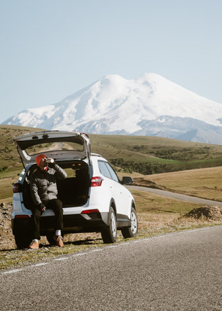 tourist rest - a man sits in the trunk of his car on the side of the road in the mountains, a beautiful landscapeの写真素材