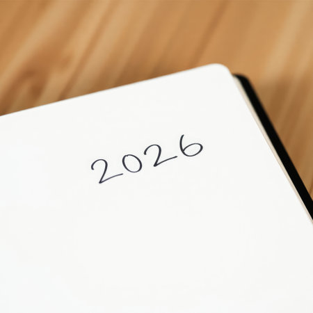 A clean, minimalist notebook page with the year 2026 prominently written in black, resting on a simple wooden desk. Evokes a sense of planning and anticipation for the futureの素材