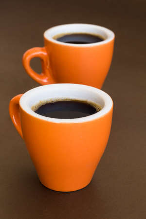 Two modern orange cups of coffee on a brown surfaceの写真素材