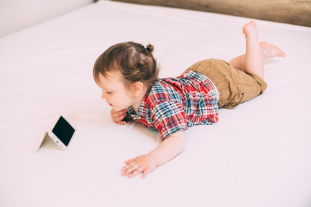 Cute little boy lies on the bed using mobile phoneの写真素材