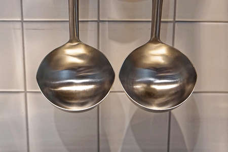 Two stainless steel soup ladles hanging in kitchen