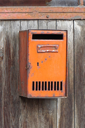 Rusty orange mailbox at wooden fence old house