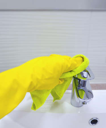 The hand of the person doing the cleaning wipes the faucet with a washcloth for a washbasin in...