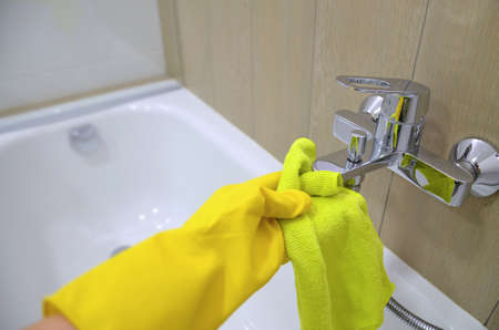 The hand of the person doing the cleaning wipes the faucet with a washcloth for a washbasin in...