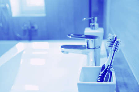 Toothbrushes in a white glass, dispenser with soap, a washbasin with a tap on the blurred background...