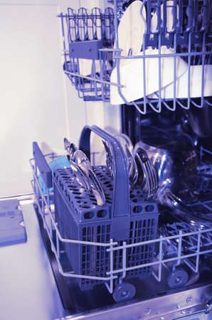 Open dishwasher with clean dishes in the white kitchen, side view. Image