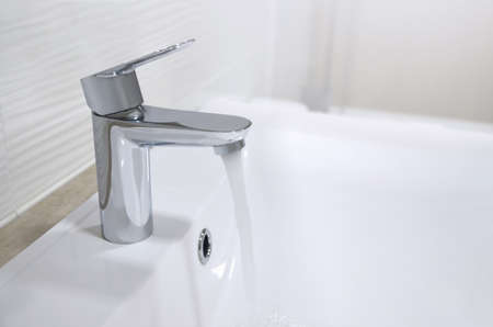 Sink with a chrome tap from which a stream of water flows, white washbasin. Image
