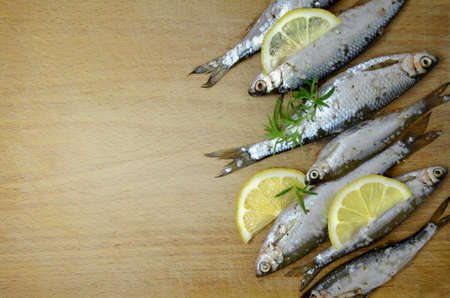 Several small fish with lemon slices and green sprigs of rosemary on a wooden cutting board. Free space, top view. Imageの写真素材