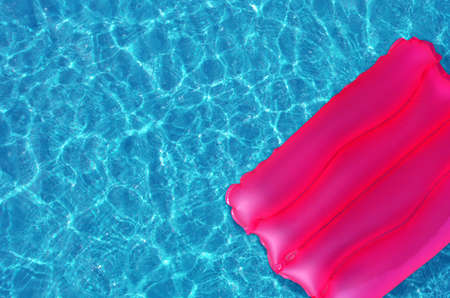 Pink inflatable mattress floating on the surface of the water. Pink lilo and summer accessories,...