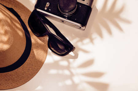 Sunglasses, hat, camera on a light background under the shadow of palm leaves, vintage photography, the concept of vacation, travel. Top view with copy space. Flat lay. Imageの写真素材