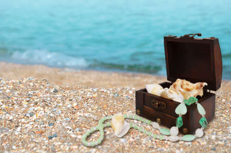 Wooden chest with summer treasures beads and shells on the background of a sandy beach and the sea. Maritime background with free space. Imageの写真素材