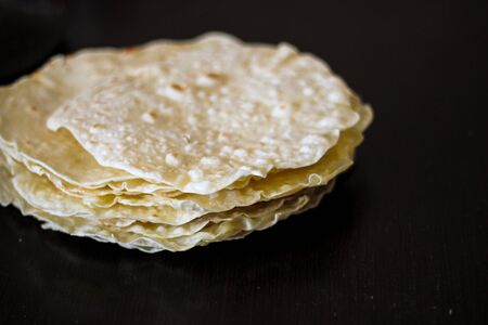Blurred shot of homemade round tortillas stack on black table background, side view. Tortilla, lavash, flatbread or pita made of wheat flour, ingredient for cooking burrito, taco, quesadilla, sandwichの写真素材