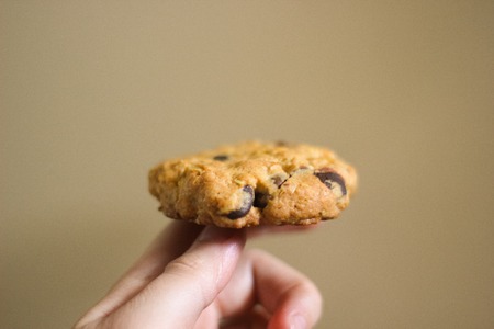 Hand holding oatmeal cookie on finger. Play heads or tails with tasty brown homemade oatcake with chocolate dropsの写真素材
