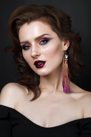 Portrait of beautiful young woman with professional makeup, perfect skin, wavy hair, long earrings. Trendy colorful smoky eyes.の写真素材