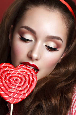 Close up portrait of beautiful young model with professional makeup, perfect skin and big red candy. Trendy eyelines and red lips. Retro styleの写真素材