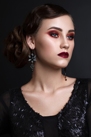 Portrait of beautiful young model with professional colorful makeup, perfect skin, red lips, retro hairdo in black clothes on dark background. Trendy colorful smoky eyes. Retro styleの写真素材