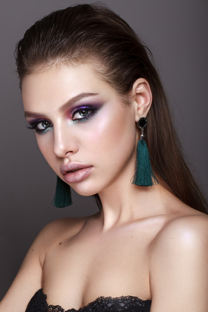 Beautiful young model with fashion make up, perfect skin, long earrings and wet hair. Trendy colorful smoky eyes.の写真素材