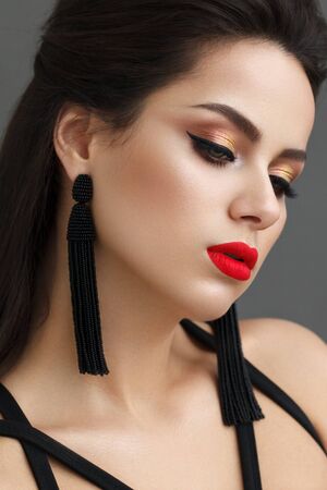 Beautiful girl with the fashion make-up, red lips, long black earrings and black arrowsの写真素材