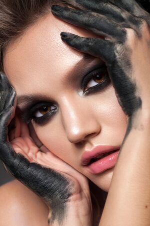Attractive young girl with black smoky eyes, dirty black fingers near the face. Halloween makeup.の写真素材