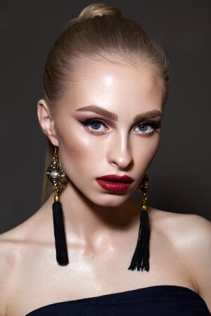 Beautiful young blond model with professional makeup, perfect skin, long fashion earrings and ponytail hairstyle.の写真素材