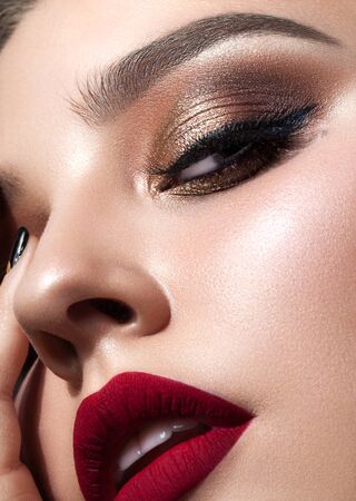 Beautiful young model with evening make up, perfect skin. Trendy golden eye-shadows and ideal red lips. A very close up photo of a high quality.の写真素材