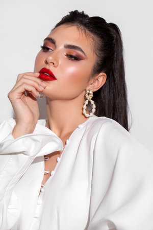 Young model with professional makeup, perfect skin, long dark hair in a white blouse. Trendy look with red lips.の写真素材