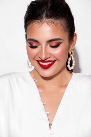 Young smiling model with professional makeup, perfect skin, long dark hair in a white blouse. Trendy look with red lips.の写真素材