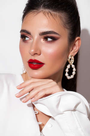 Young model with professional makeup, perfect skin, long dark hair in a white blouse. Trendy look with red lips.の写真素材