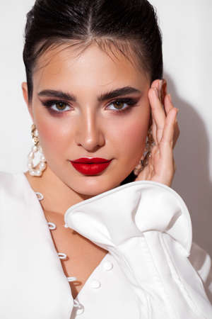 Young model with professional makeup, perfect skin, long dark hair in a white blouse. Trendy look with red lips.の写真素材