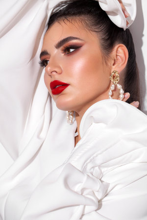 Young model with professional makeup, perfect skin, long dark hair in a white blouse. Trendy look with red lips.の写真素材