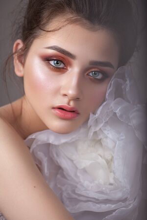 Attractive young girl with bright colorful trendy smoky eyes, who hugs a big white air flower. Morning fresh look.の写真素材