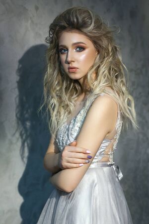 A beautiful girl with professional colorful makeup and volume hairstyle. White bridal dress and grey background.の写真素材