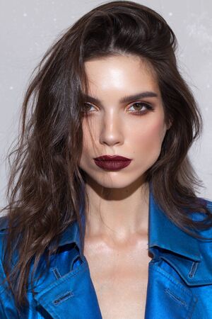 Portrait of a beautiful brunette girl with hazel eyes and square jaw and chin. Perfect skin, dark red lips, blue coat.の写真素材
