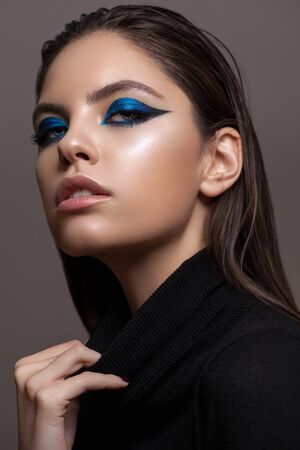 Portrait of a beautiful girl with professional makeup, ideal skin, bright blue graphic smokey eyes and in black sweaterの写真素材