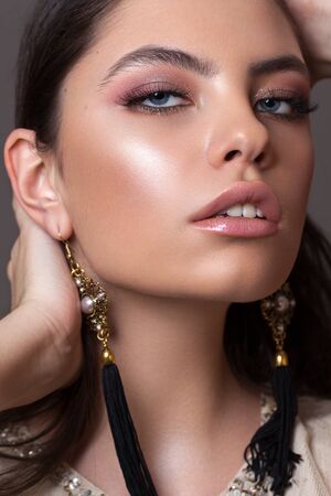 Close up portrait of a beautiful girl with professional makeup, ideal skin, rose eyeshadows and lips and long earringsの写真素材