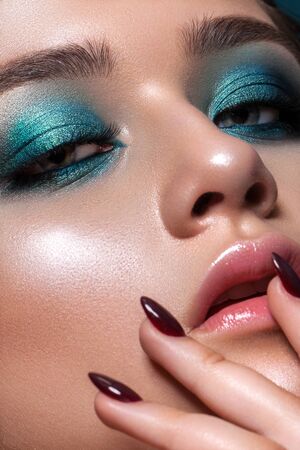 Close up photo of a beautiful young model with bright blue trendy smoky eyes, blue eyes, perfect skin and natural lips. Girl touches her lips with her hand. Red manicure.の写真素材
